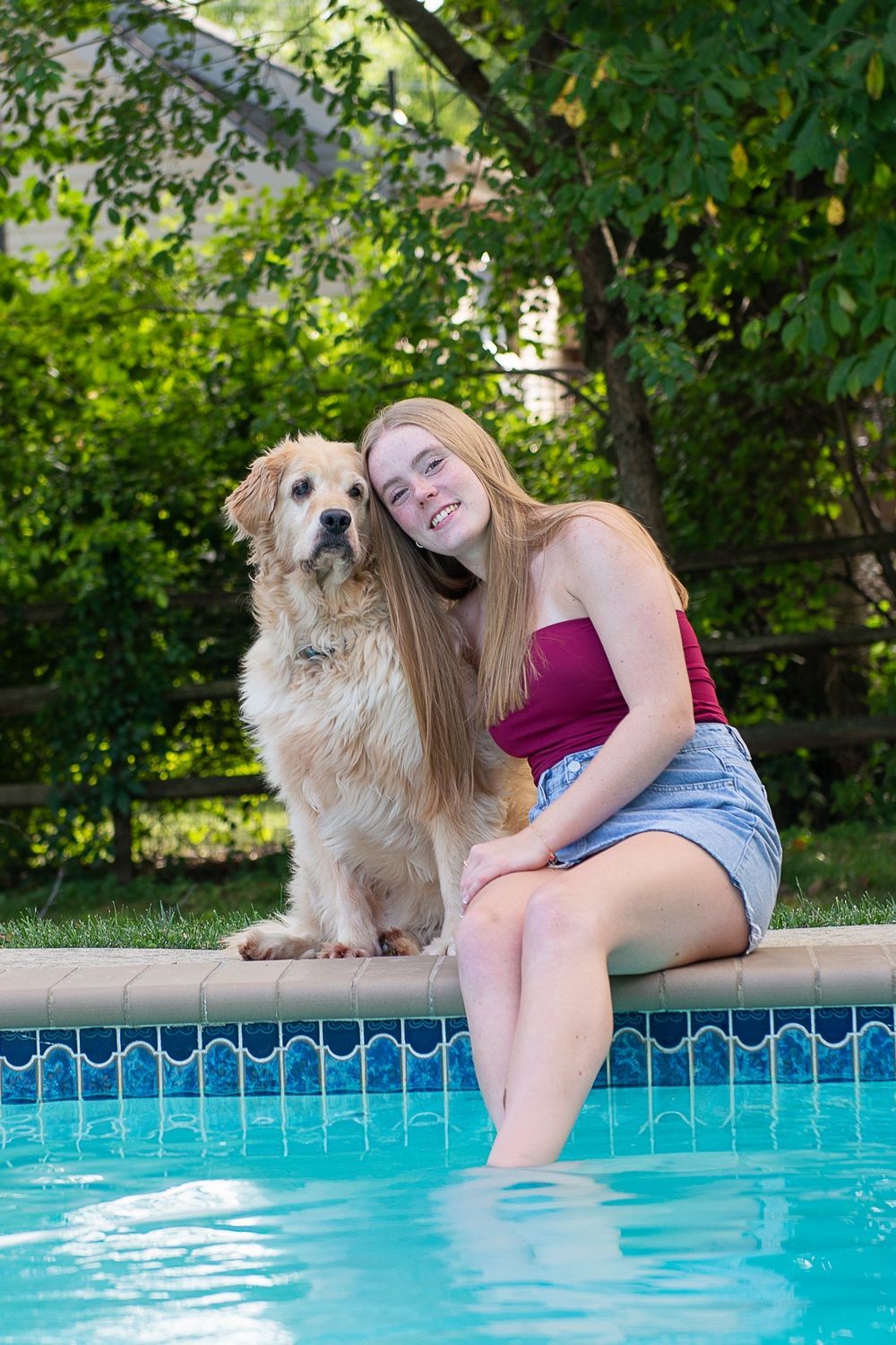 A person and golden retriever relax by a swimming pool on a sunny summer day.