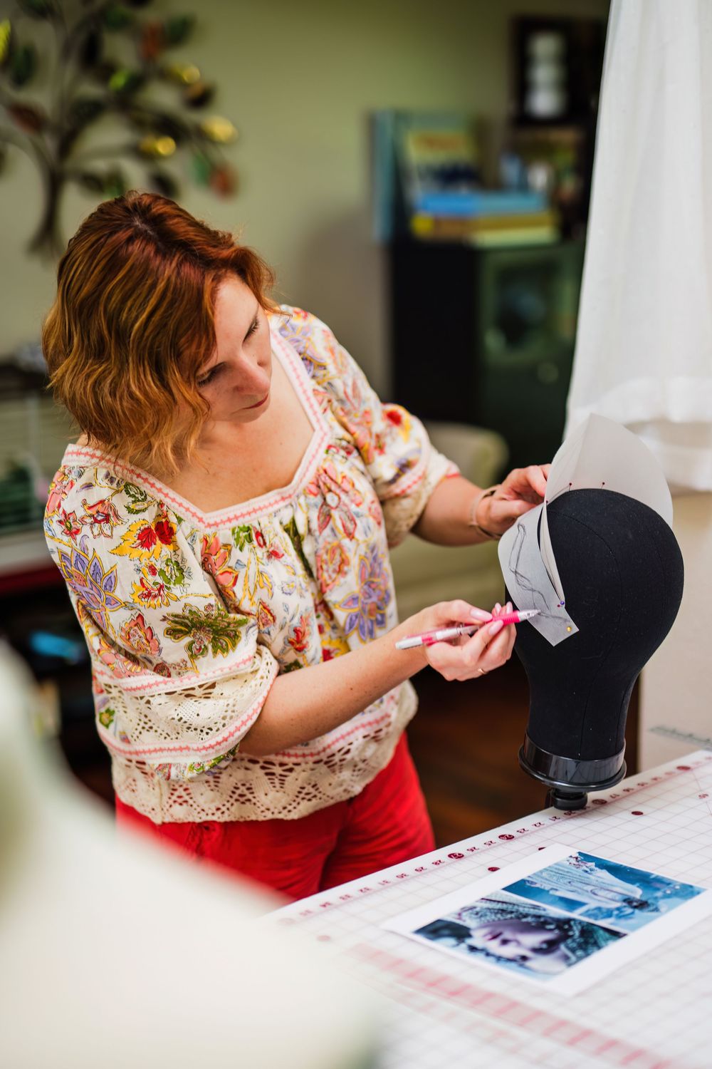 Someone in a floral top works carefully on a sewing project at a well-lit desk.