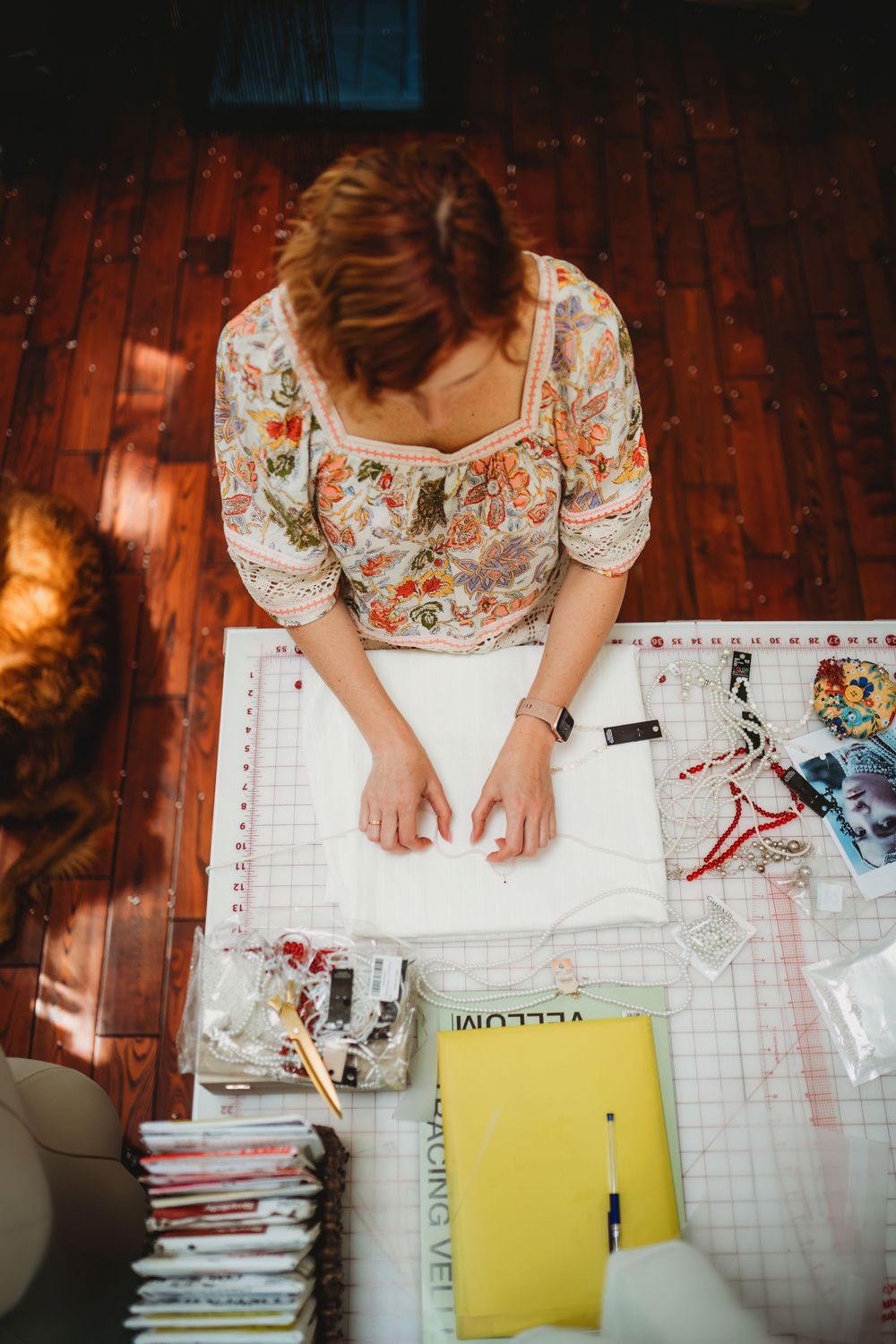 Overhead view of someone in a floral dress working at a desk with papers and supplies.