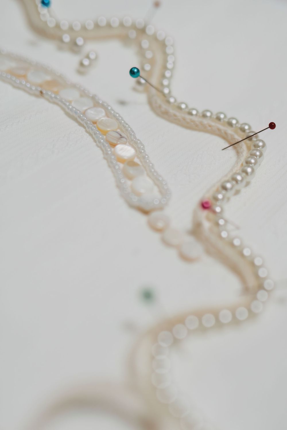 Delicate pearl pins arranged in a curved line on a soft white surface create an elegant composition.