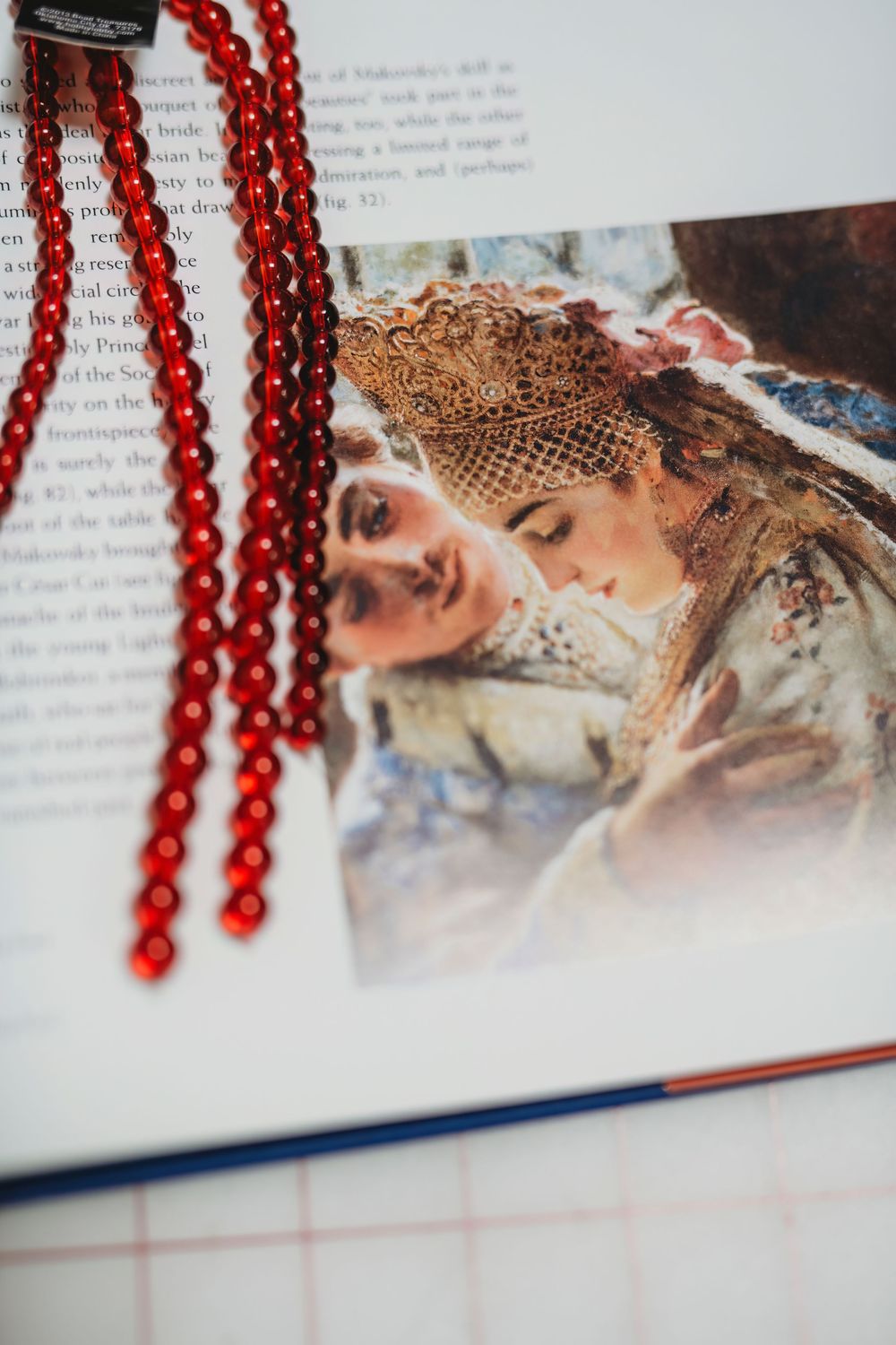 Red beaded necklace draped over an open book page with classical artwork illustrations.
