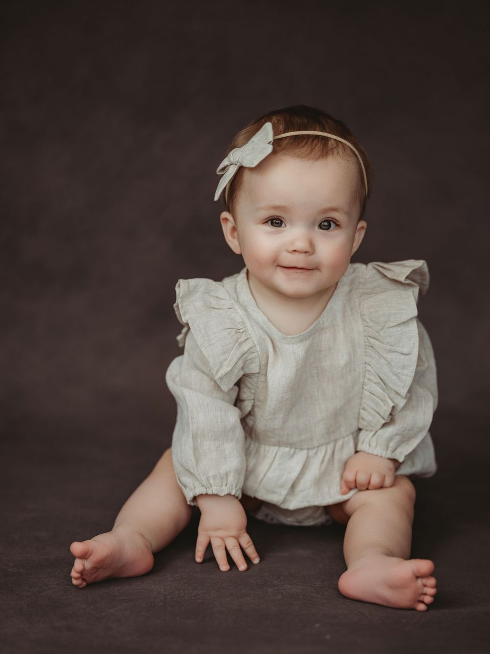 A baby in a white ruffled outfit lies on a dark backdrop showing tiny hands and feet in a series of artistic poses.