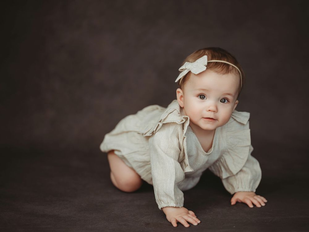 A baby in light colored clothing crawls and plays on a dark backdrop in a series of connected photos.