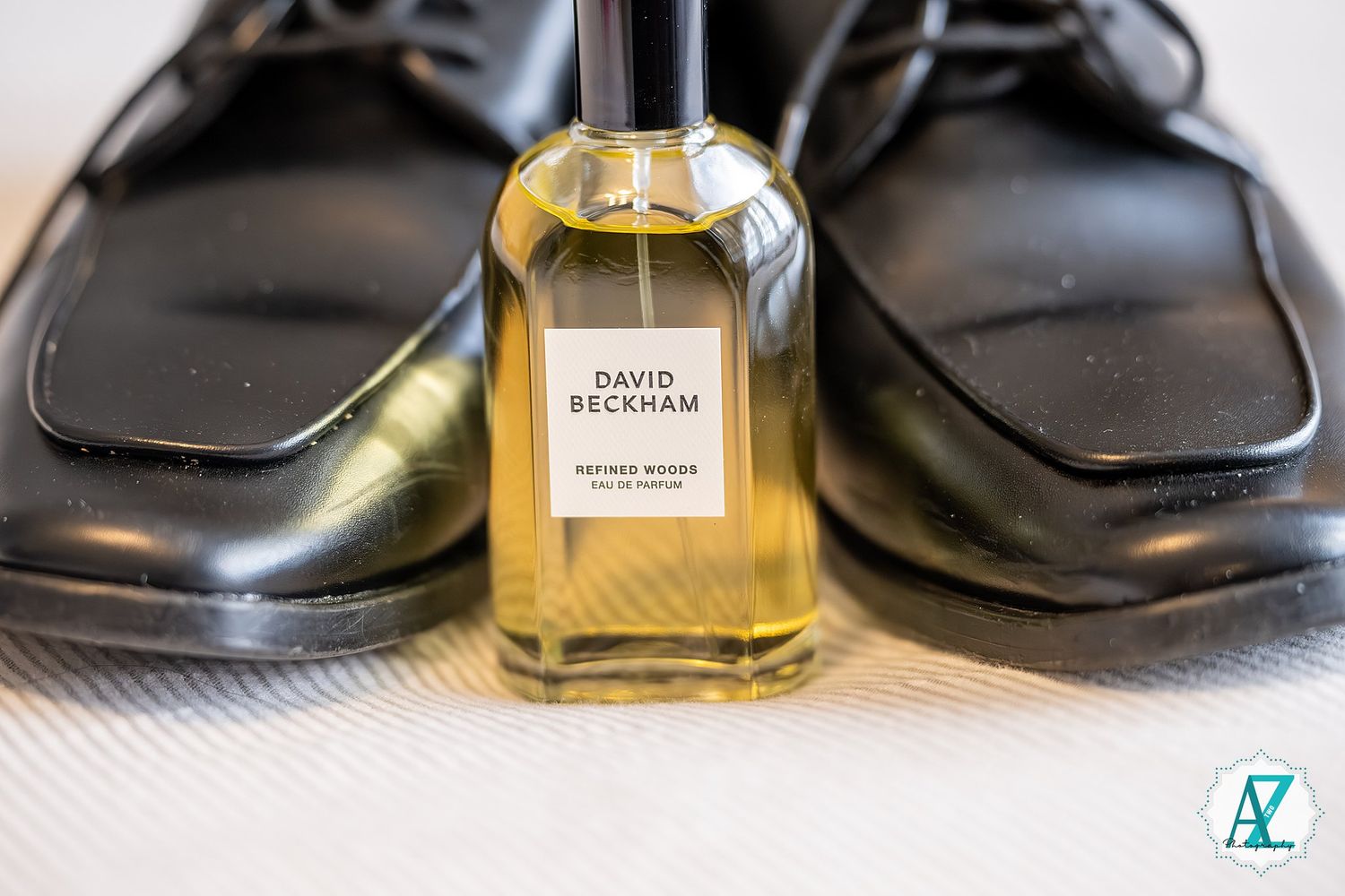 Black leather dress shoes arranged with a bottle of luxury perfume on a textured white surface.