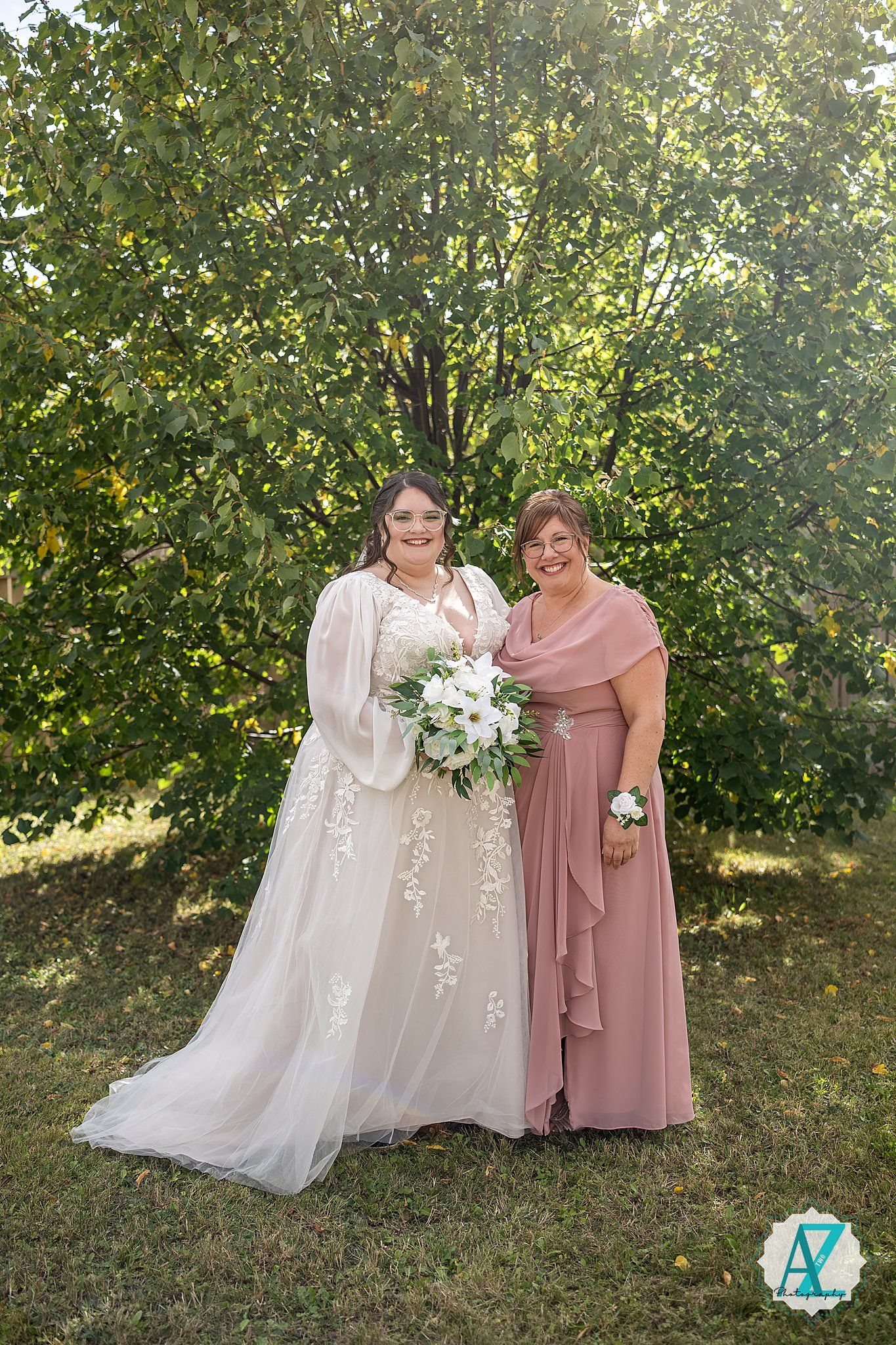 A wedding portrait showing two people in formal attire standing outdoors with a beautiful white floral bouquet.