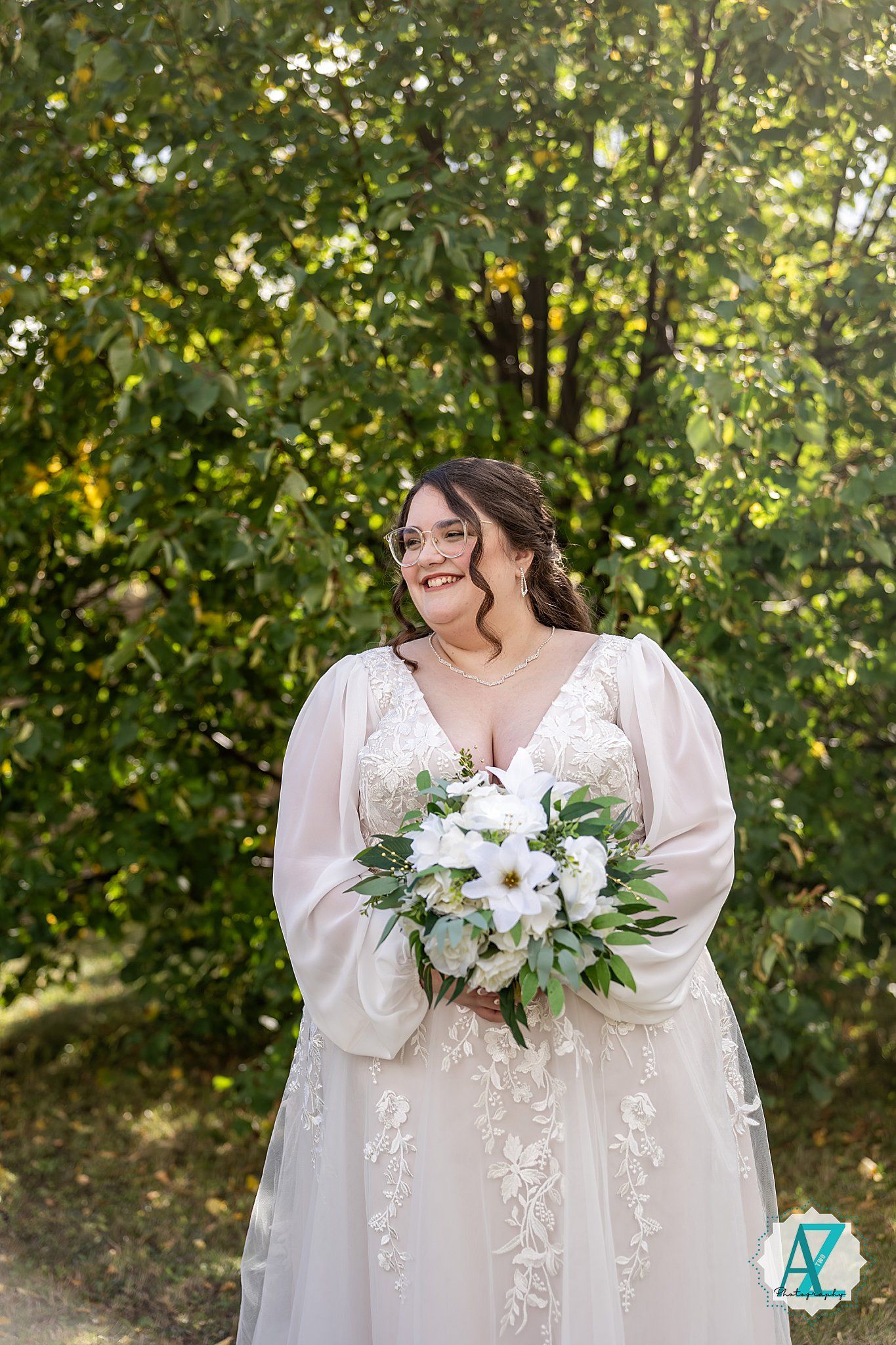 Two people in elegant white dresses share a joyful moment outdoors with a white floral bouquet.