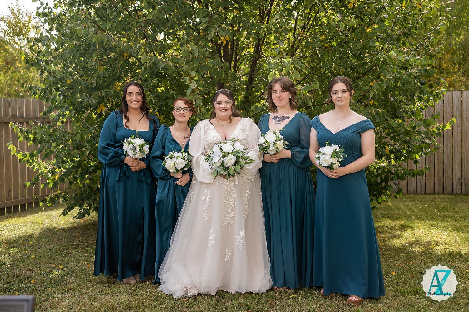 Wedding party wearing teal blue bridesmaid dresses and white bridal gowns pose together in an outdoor garden setting.