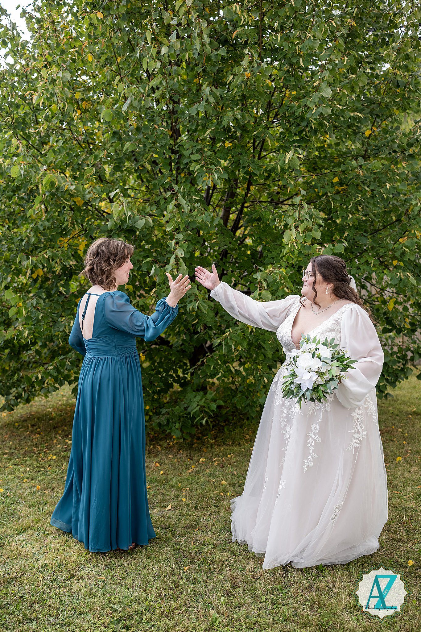 Two people in wedding attire twirl and dance together in a garden setting with green trees in the background.