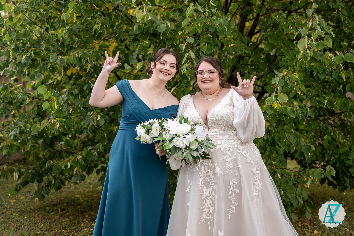 Wedding party poses playfully outdoors with bridesmaids in teal dresses and bride in lace gown.