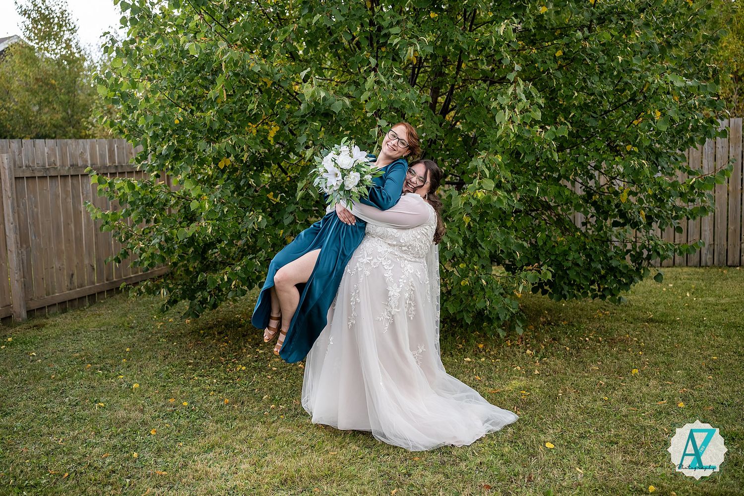 Bridesmaids in teal gowns and bride in white dress crouch together laughing during outdoor photo session.