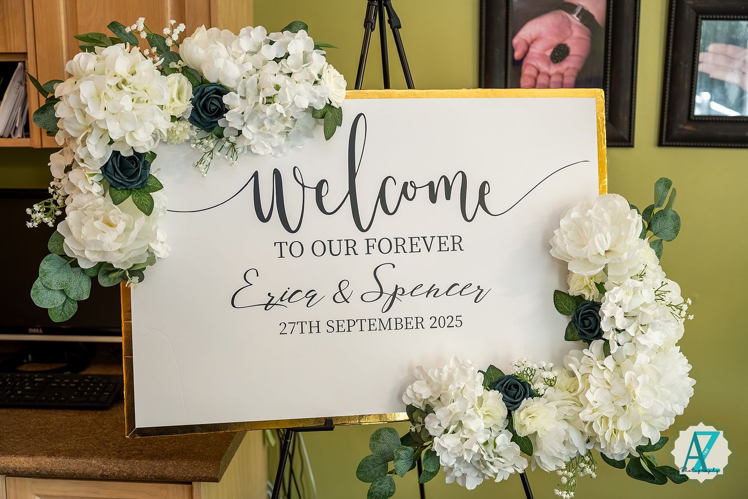 Wedding welcome sign surrounded by elegant white hydrangea floral arrangements and greenery at reception entrance.
