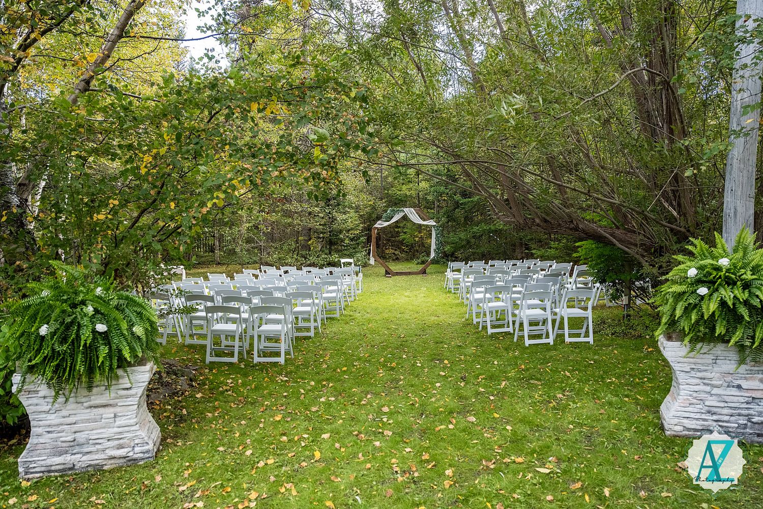 White chairs arranged in rows on a grassy lawn surrounded by trees for an outdoor wedding ceremony.