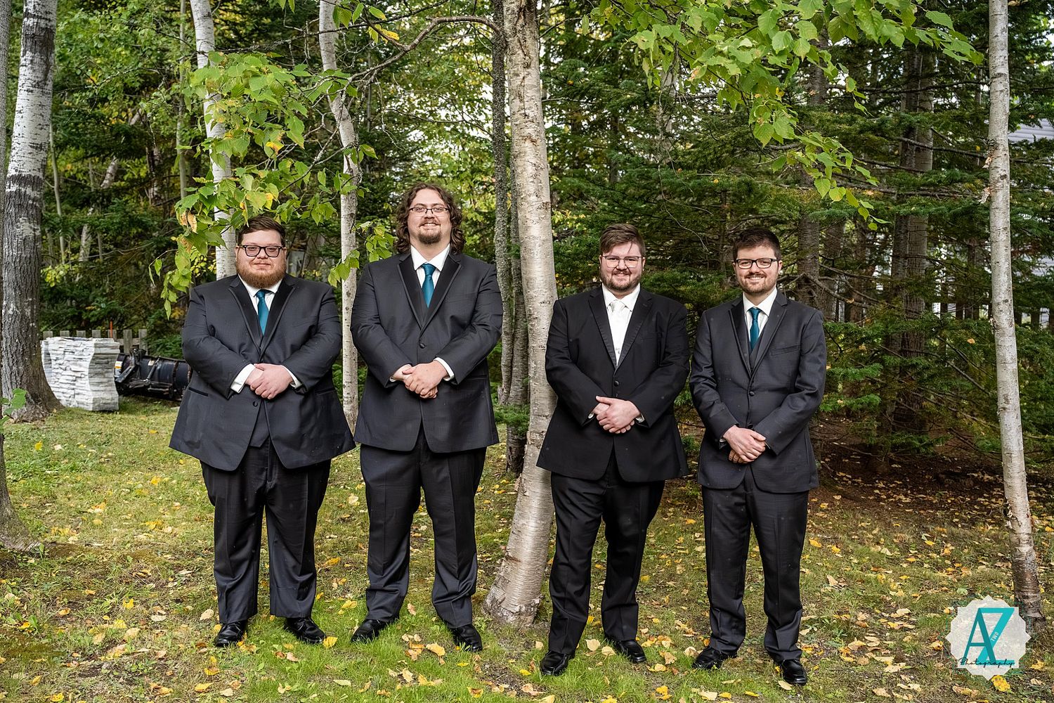 A group in formal attire poses together in front of birch trees in a woodland setting.
