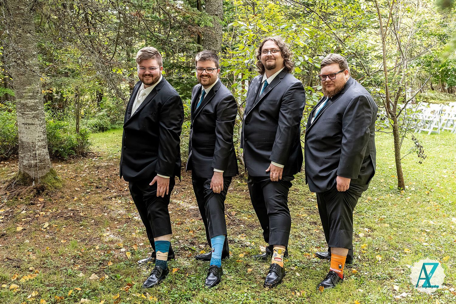Group wearing black suits and colorful socks posing together on grass near trees.
