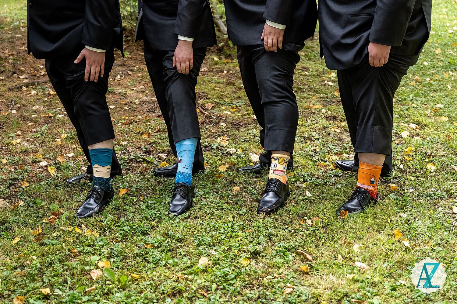Groomsmen show off colorful patterned socks while standing on grass in formal attire.