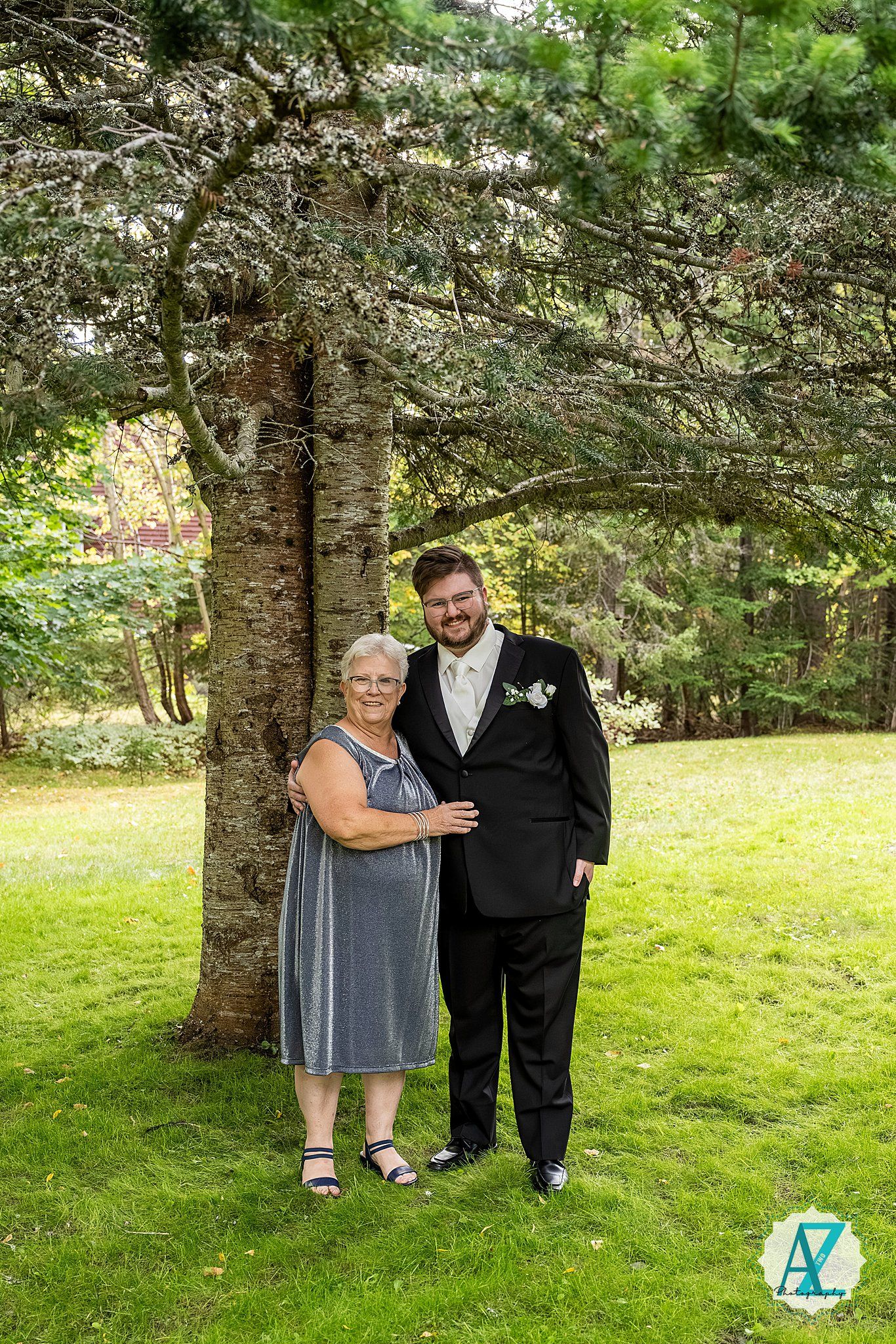 A formal portrait session in a wooded outdoor setting with pine trees and green grass in the background.