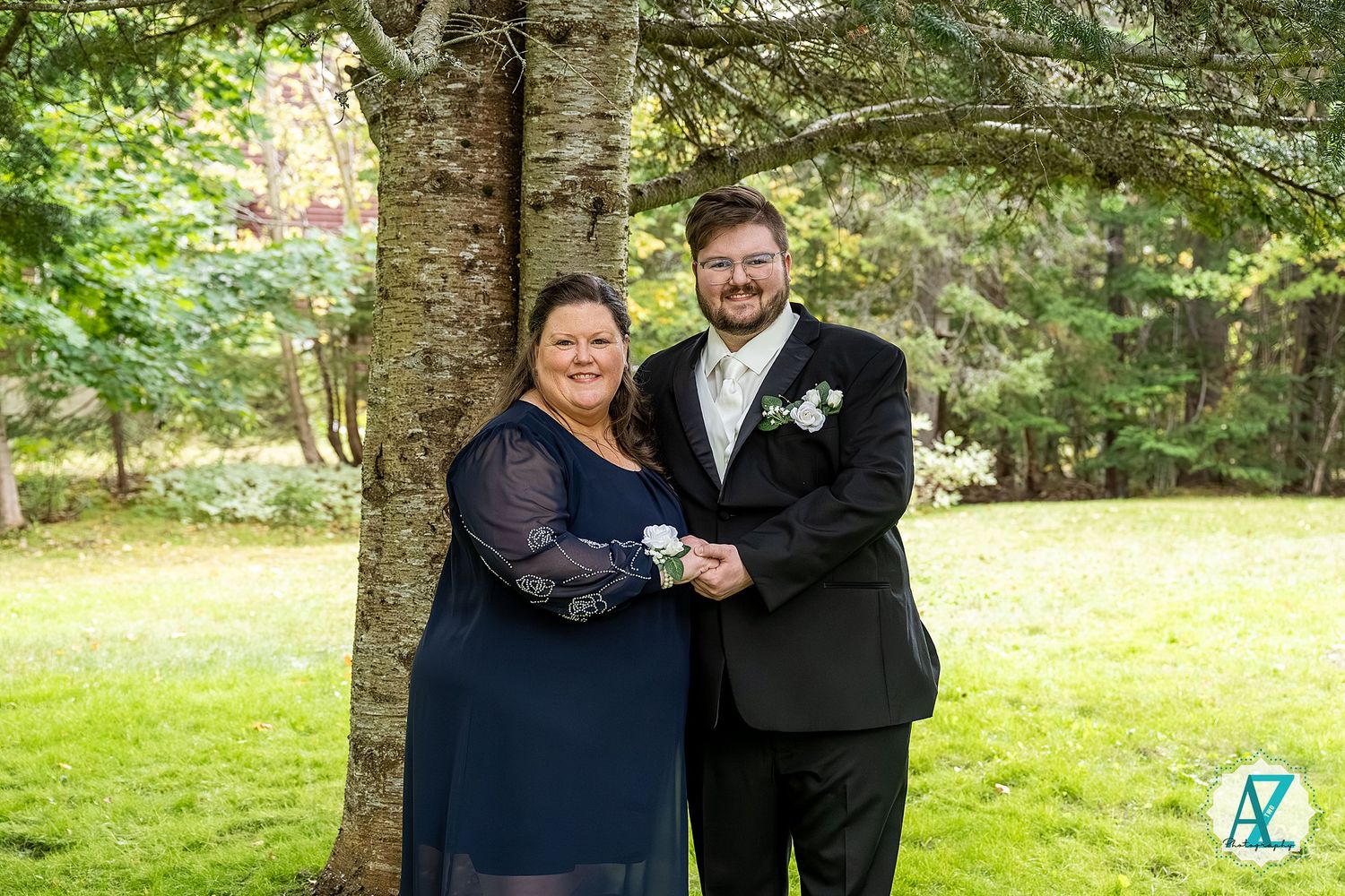 A couple in formal attire poses together in a lush garden setting during a special event celebration.