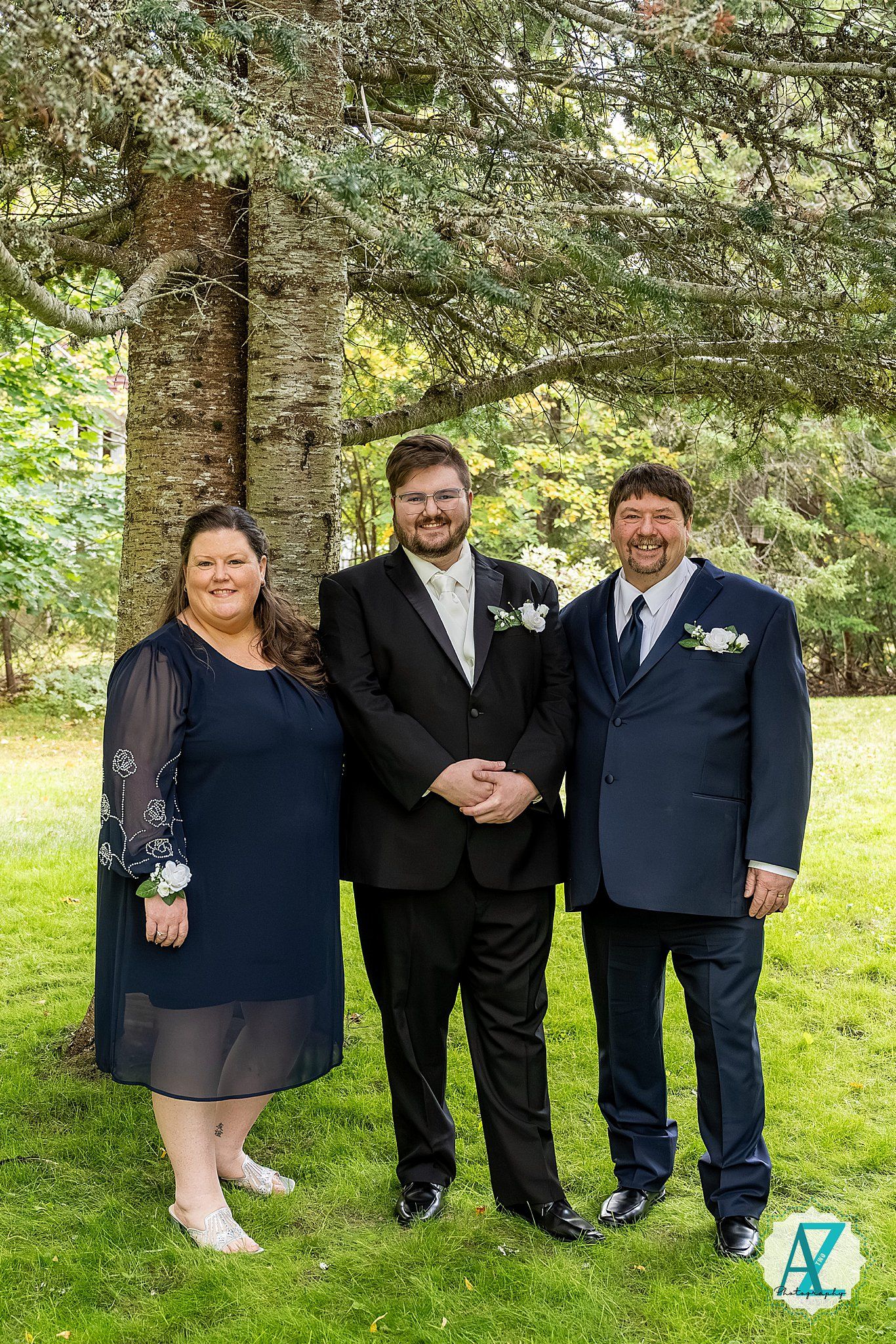 Group formal photo taken outdoors against evergreen trees on a sunny day.