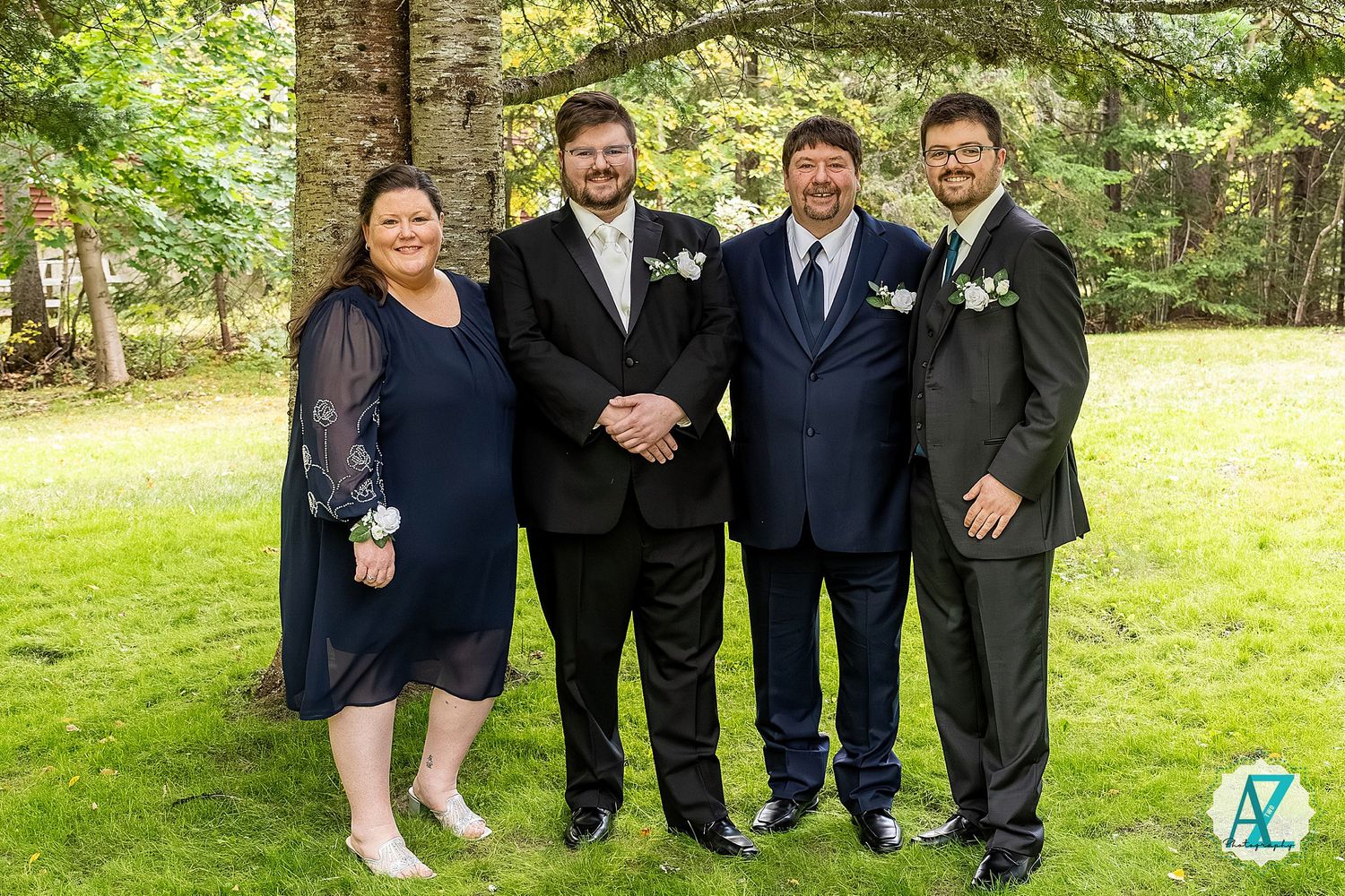 Groomsmen in black suits pose together on a sunny day in a lush green outdoor setting.