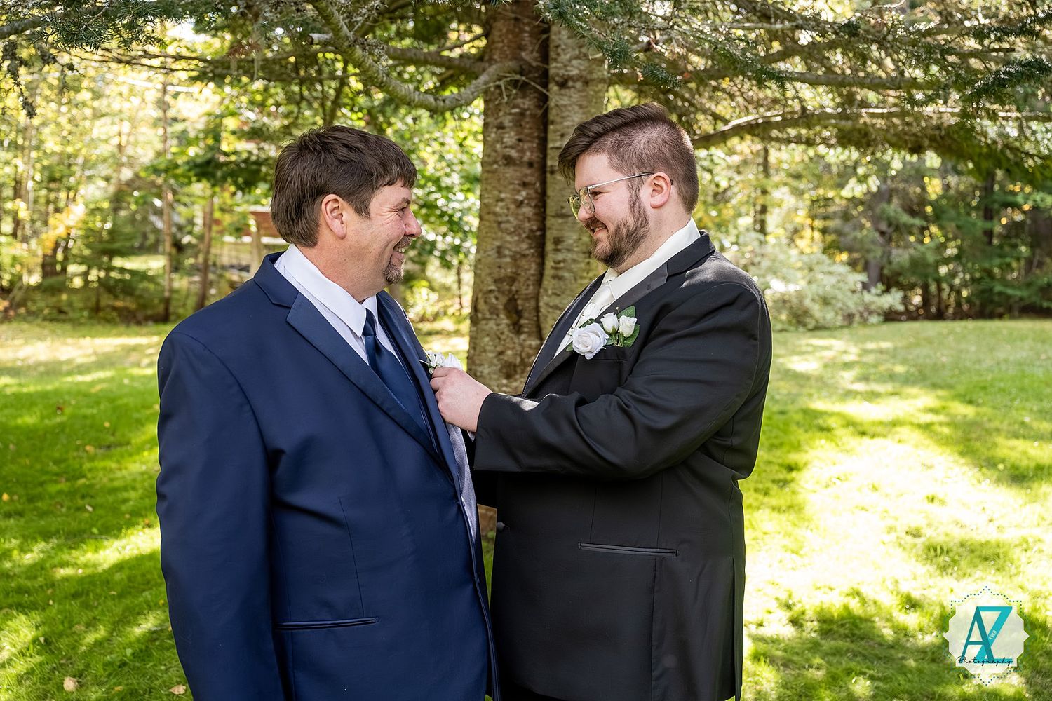 Two people sharing a candid moment while dressed formally in a sunlit forest setting.