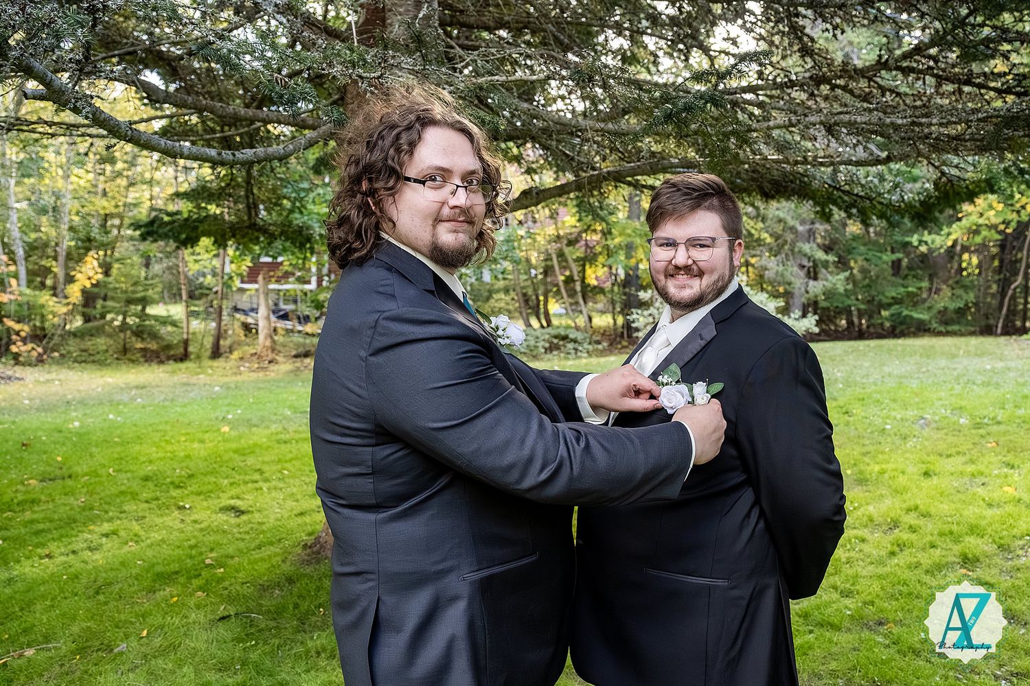 Two people in formal black attire dancing together in a lush green outdoor setting.