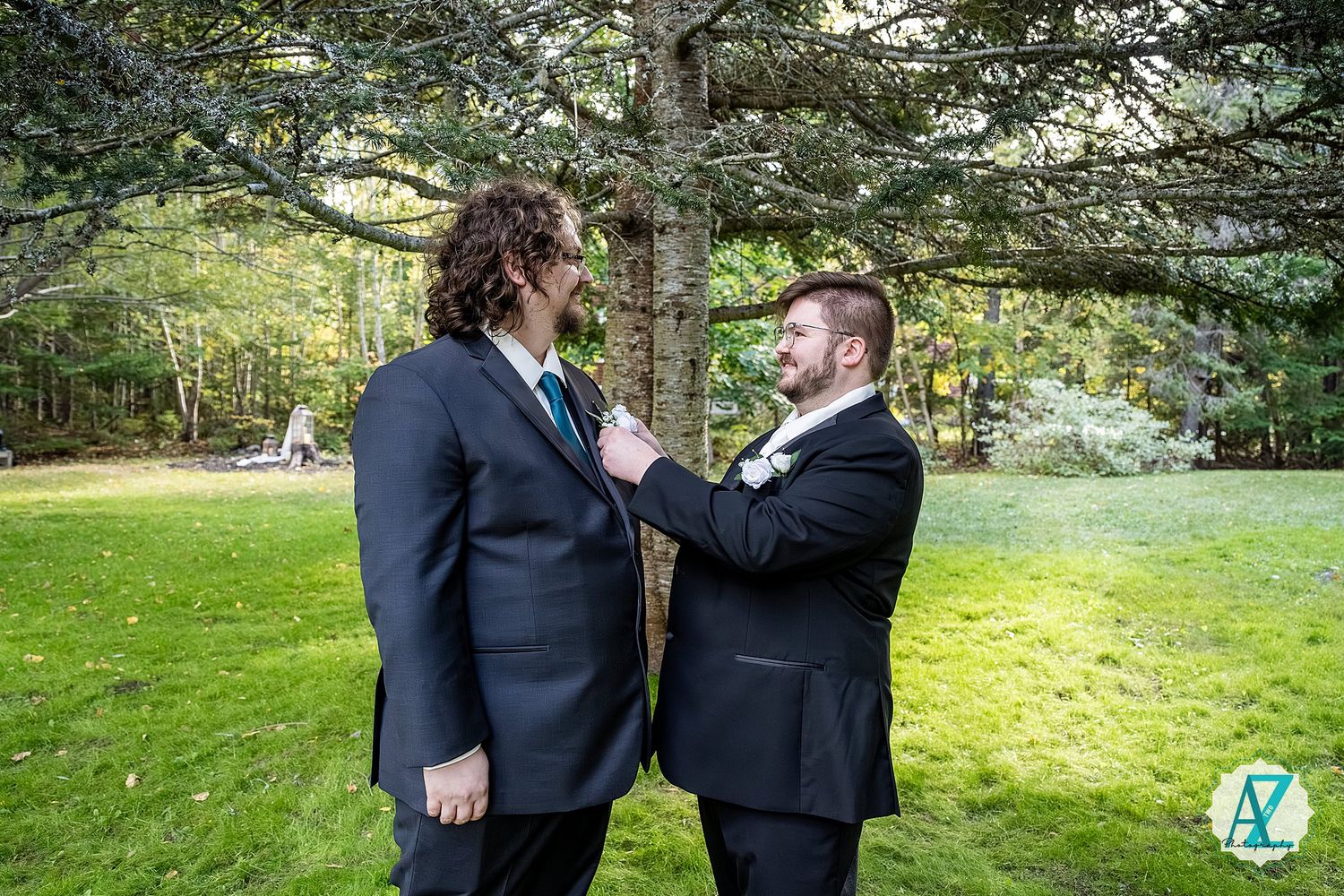 Two people in dark suits share a tender moment together in a lush green outdoor garden setting.