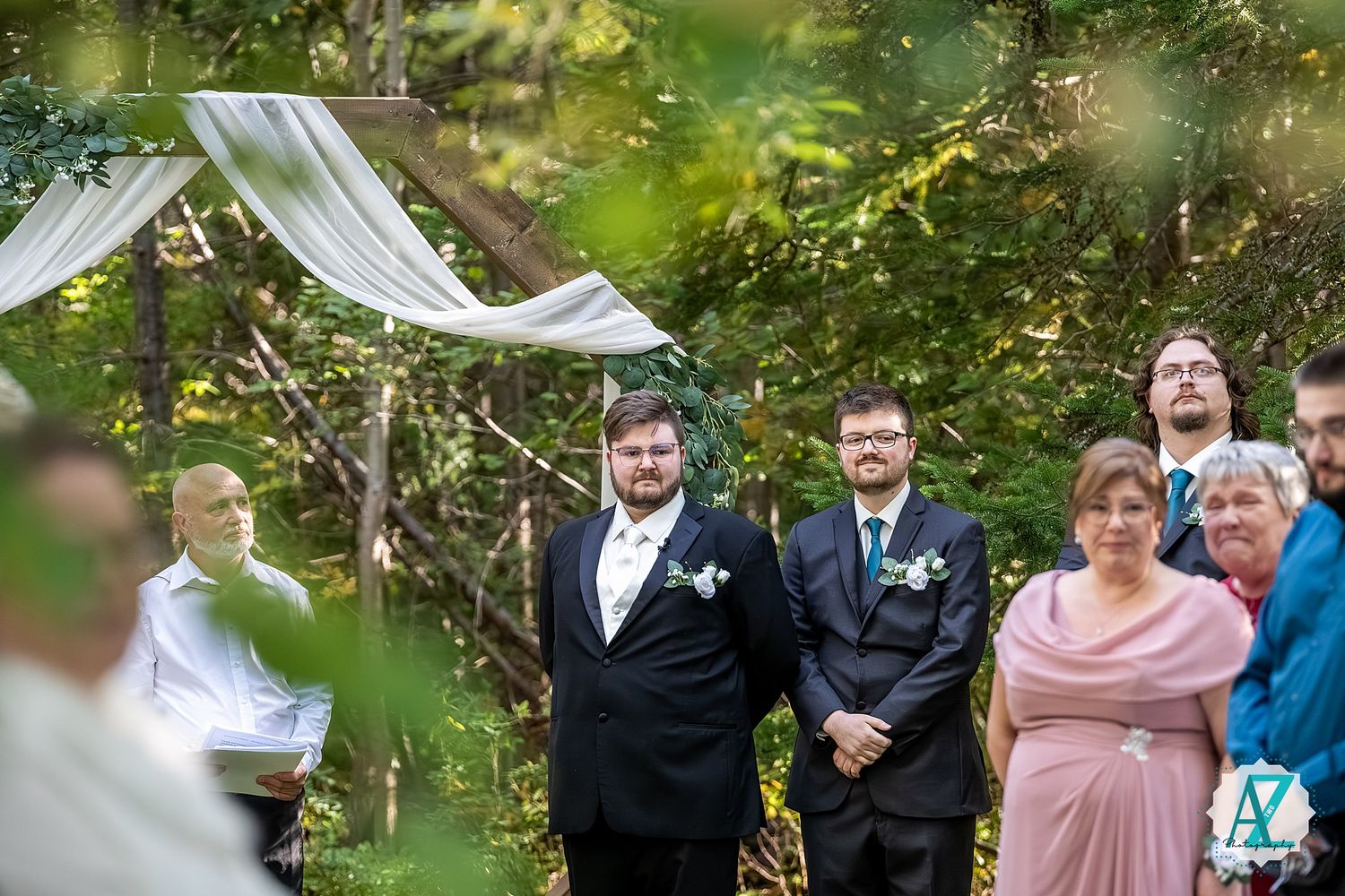 Wedding party celebrates joyfully in a natural garden setting with white draping decor.