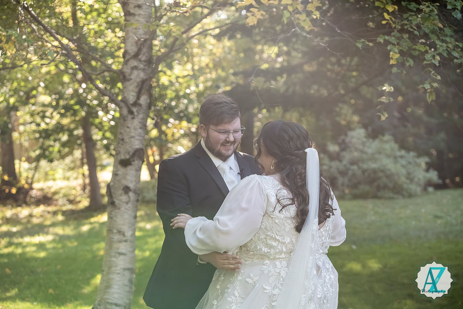 Outdoor wedding celebration in a wooded setting with sunlight filtering through trees during golden hour.