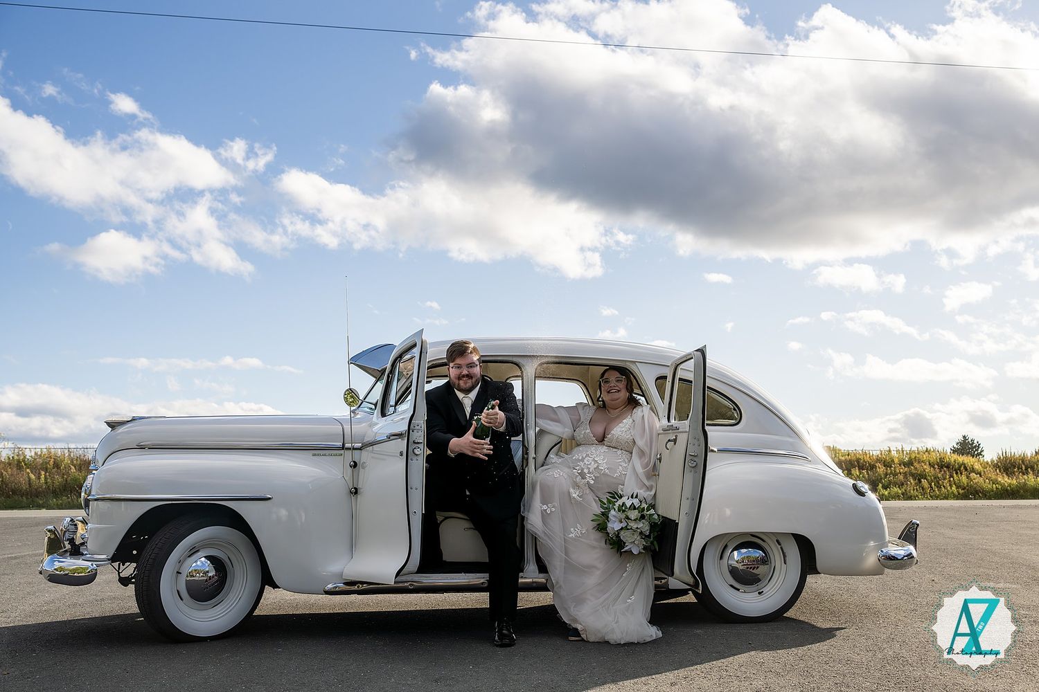 A vintage white car on a rural road with dramatic clouds in the sky creates a romantic wedding scene.