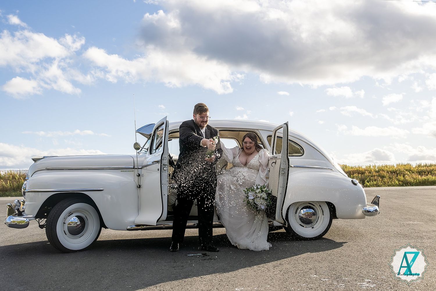 A white classic convertible car is parked on a scenic coastal road with dramatic cloudy skies in the background.