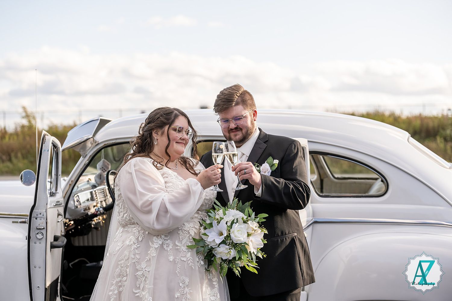 Bride and groom embrace in romantic poses through car window of vintage white automobile.