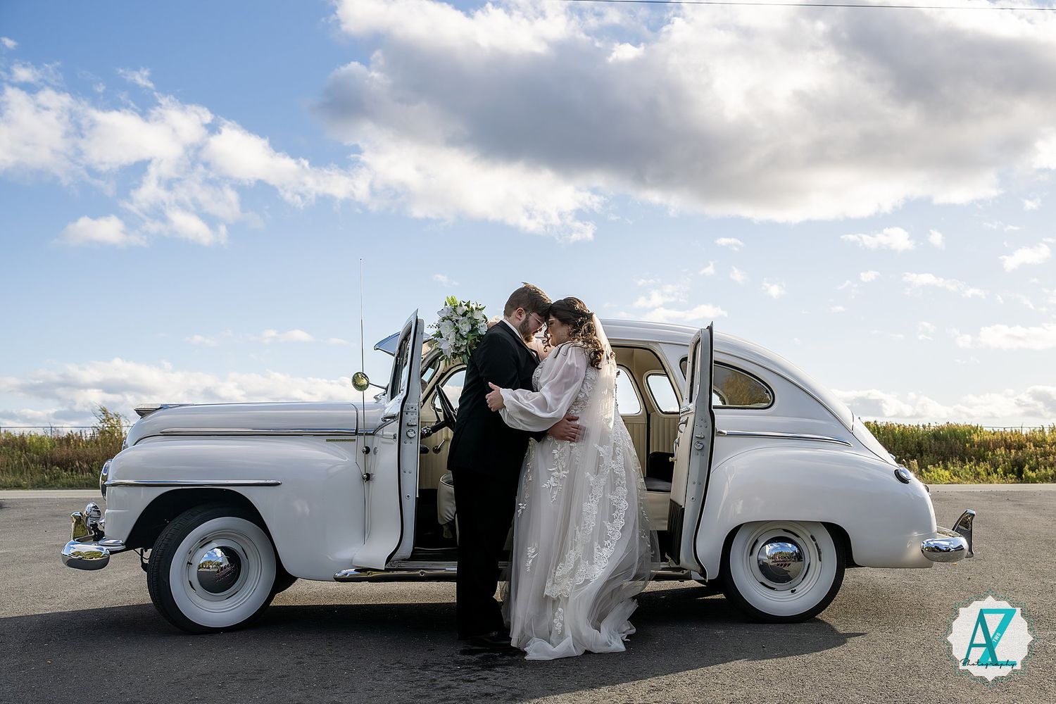 Classic white vintage car parked against a dramatic cloudy sky backdrop at a wedding.