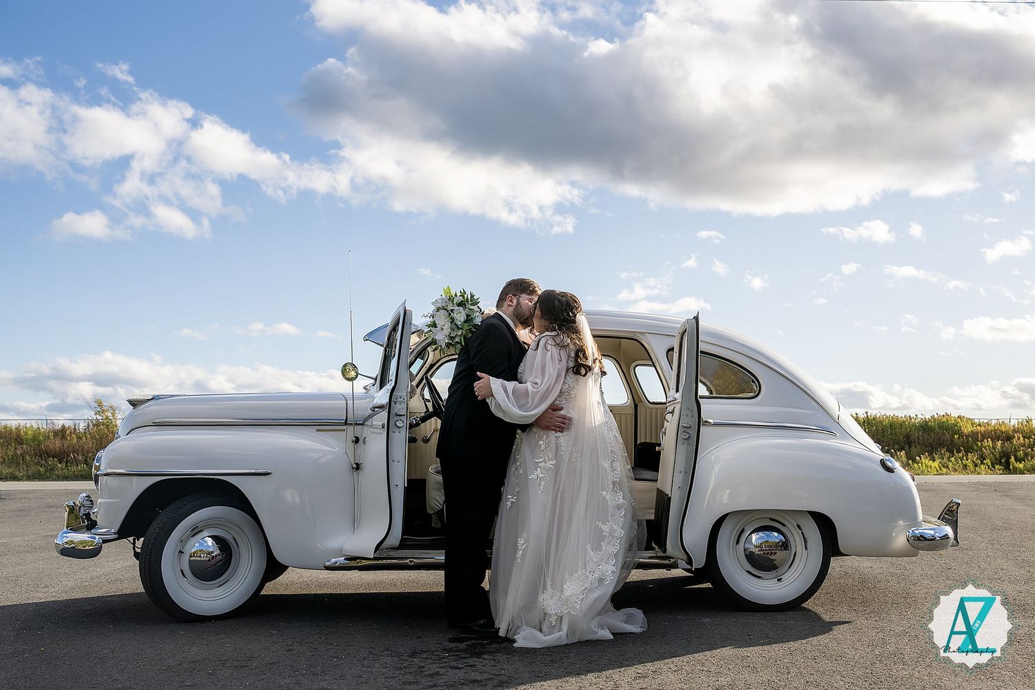 Silver vintage car photographed at sunset with couple in formal attire creating artistic wedding portraits.