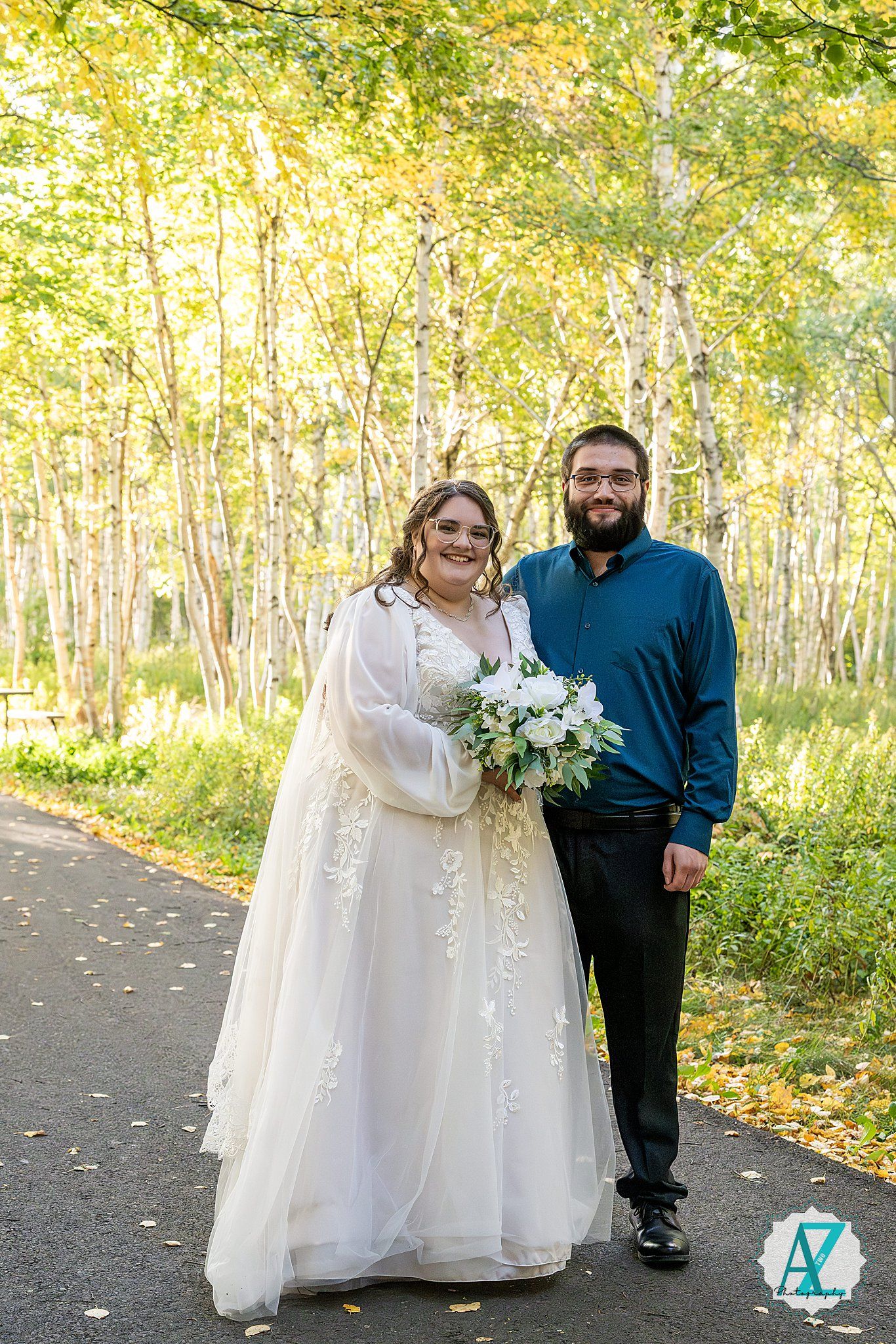 A couple poses together on a tree-lined path during an autumn wedding photo session.