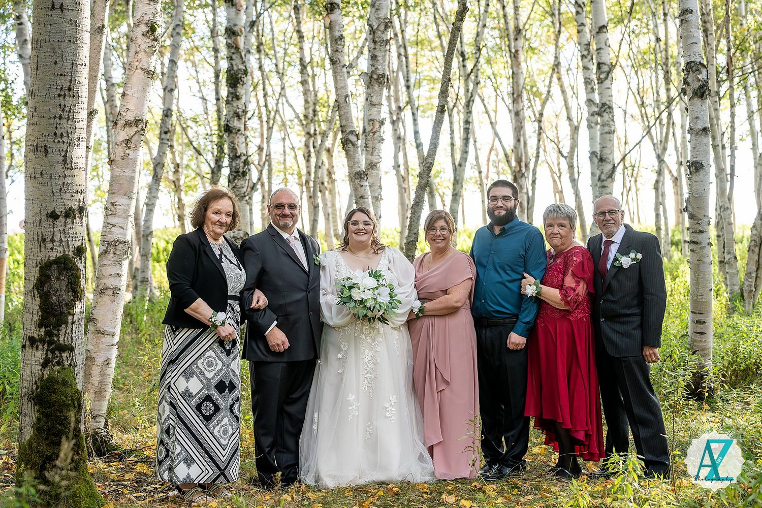 Wedding party poses together in a scenic birch tree forest setting with natural sunlight filtering through.
