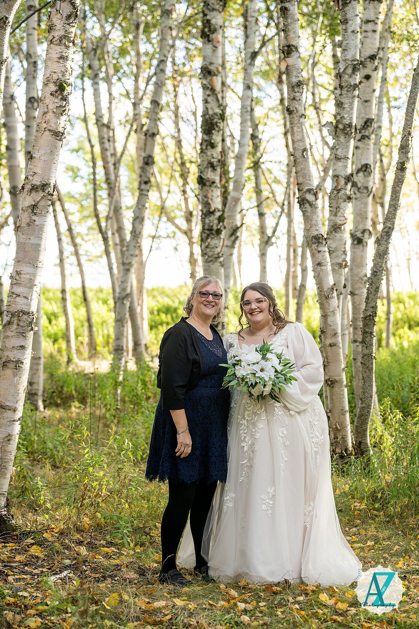 Wedding party members gather among birch trees in a sunlit forest setting.