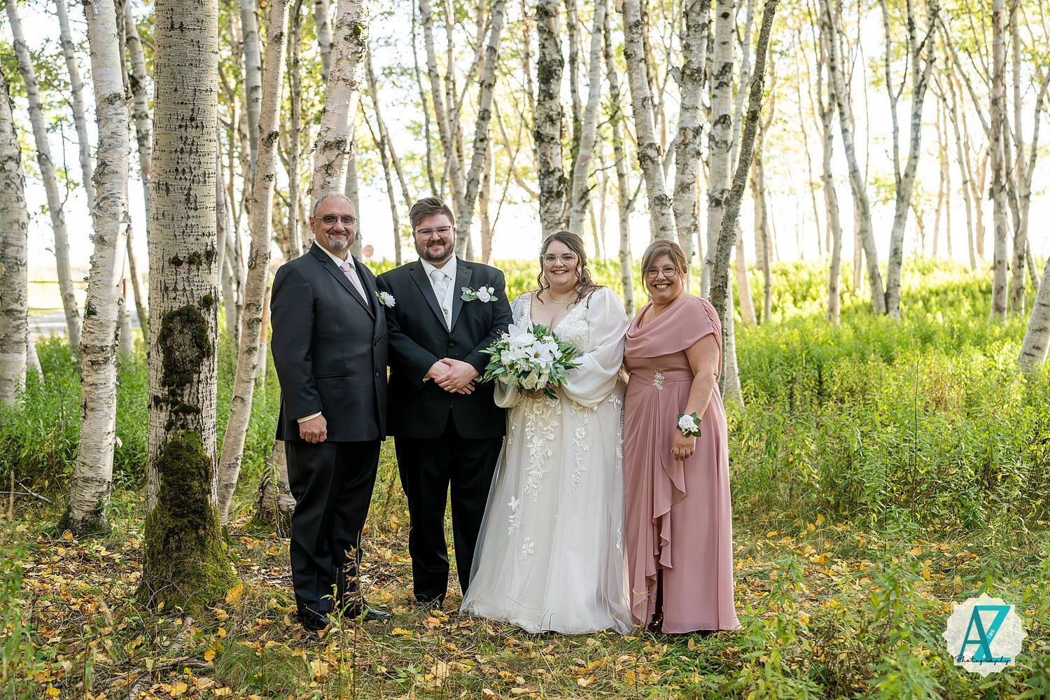 Wedding party poses in scenic birch tree forest with sunlit foliage creating a magical outdoor setting.