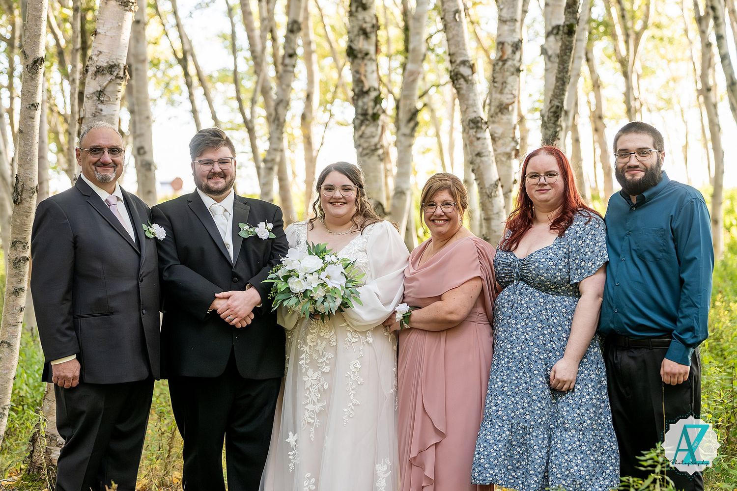 Wedding group photo in a sunlit aspen grove with guests lined up among white tree trunks.