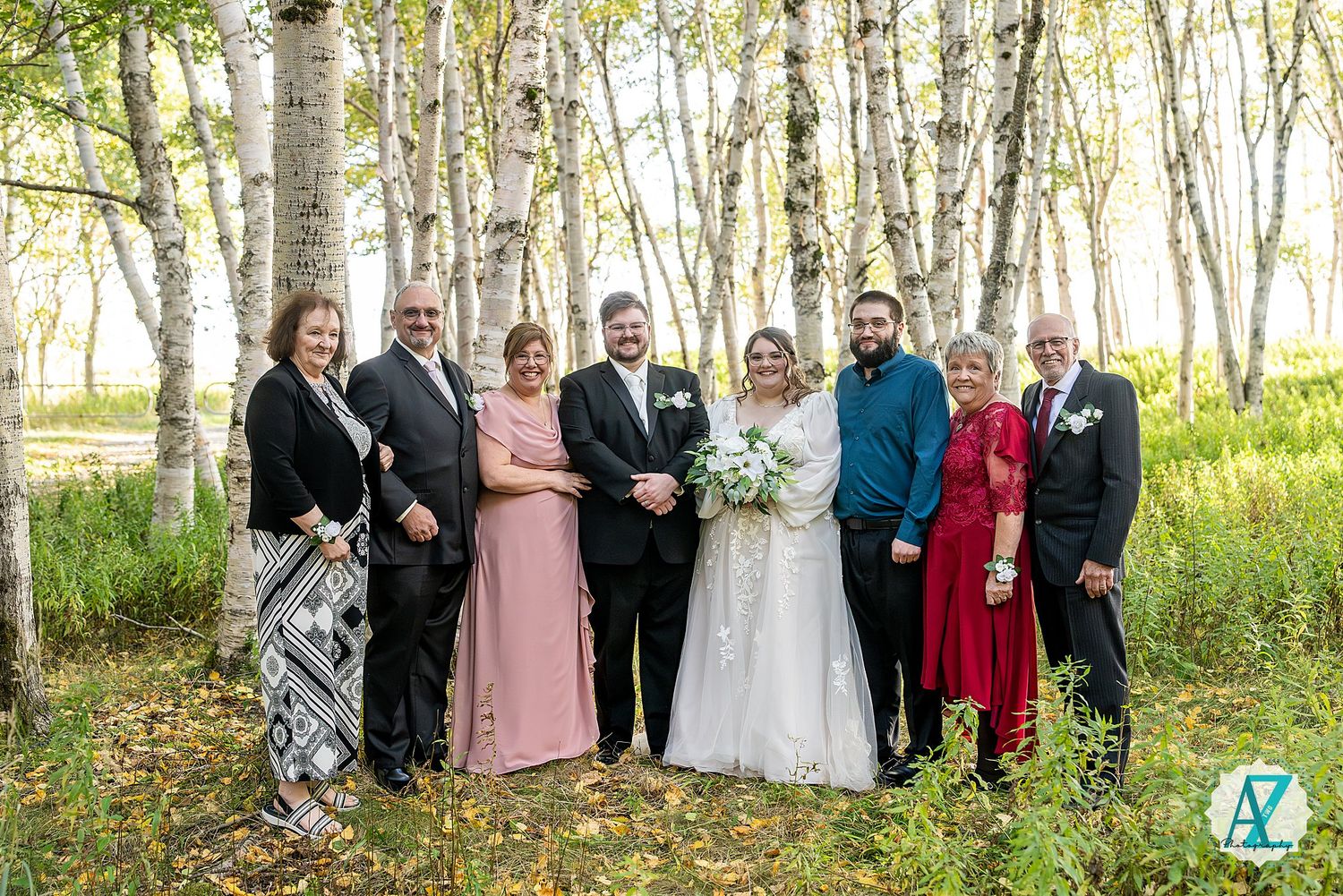 Wedding party stands in line among white birch trees in a forest setting during autumn.