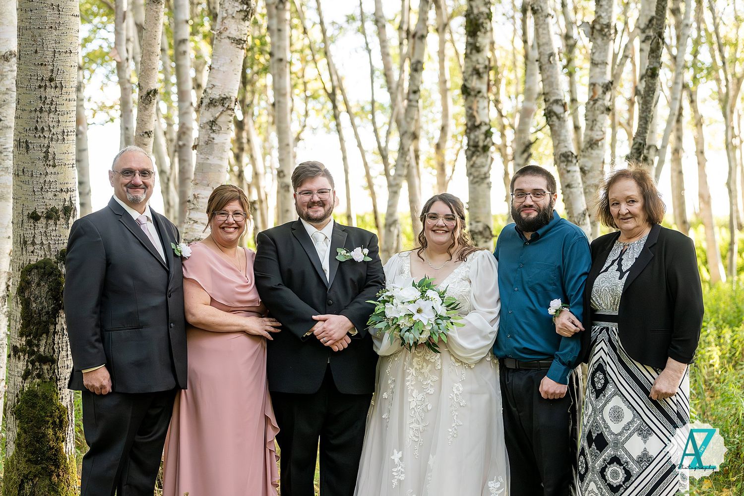 Wedding group stands among white birch trees in a beautiful forest setting during golden hour.