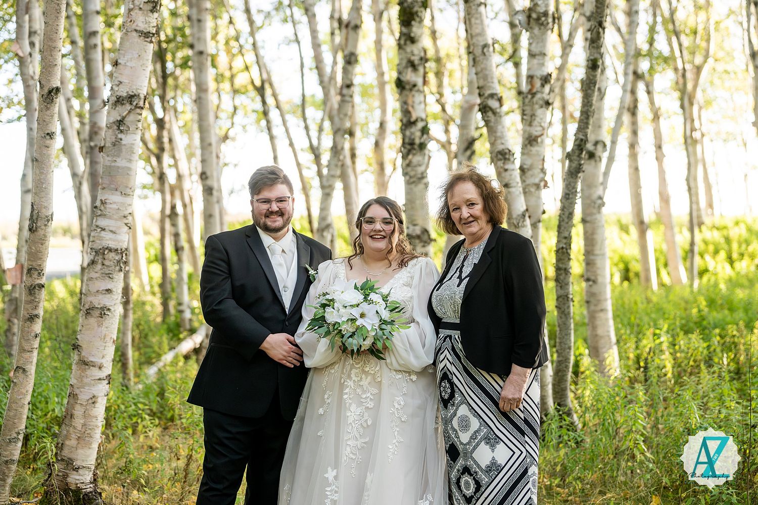 Wedding celebration group gathered among white birch trees in a natural forest setting.