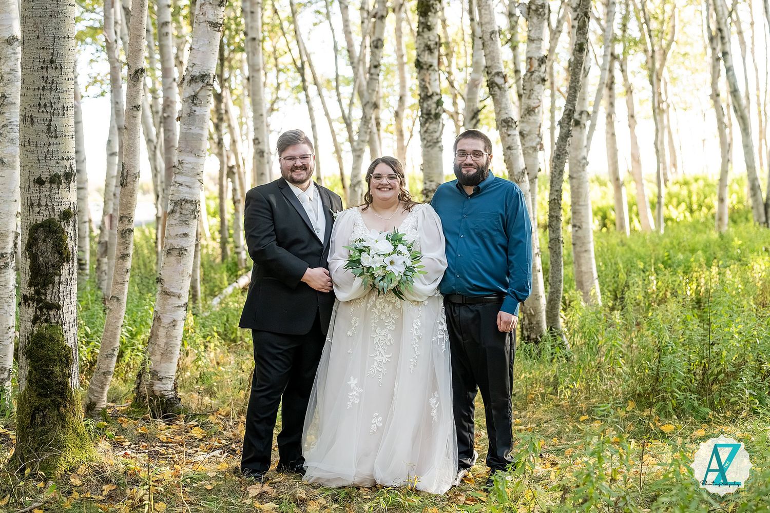 Wedding celebration group photo captured in a serene birch forest with dappled sunlight.