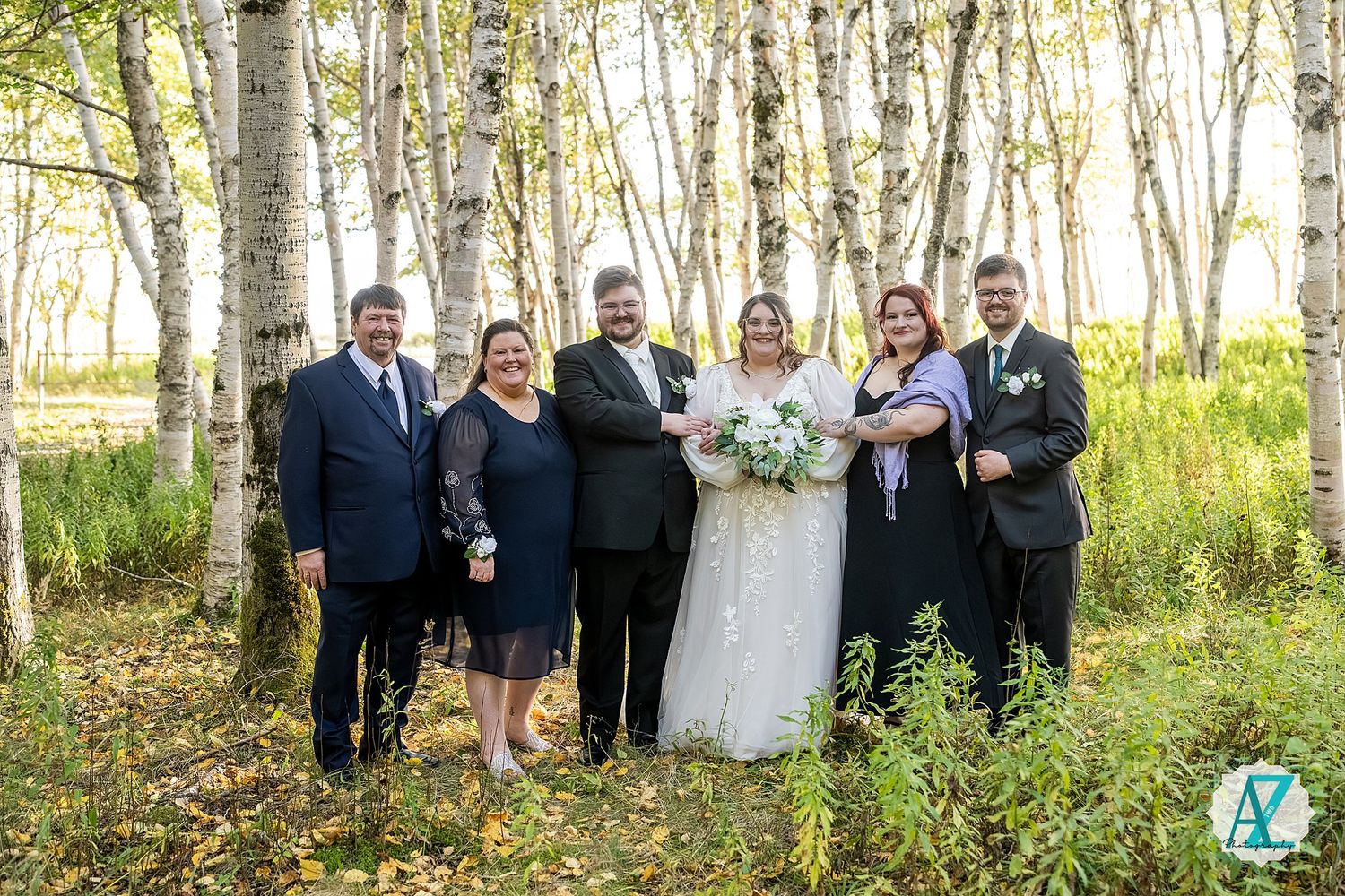 Wedding party poses together in a scenic birch tree forest during golden hour.