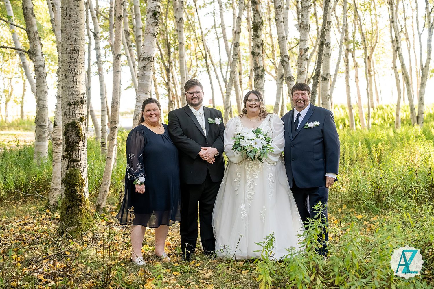 Wedding group stands among white birch trees in natural outdoor setting.