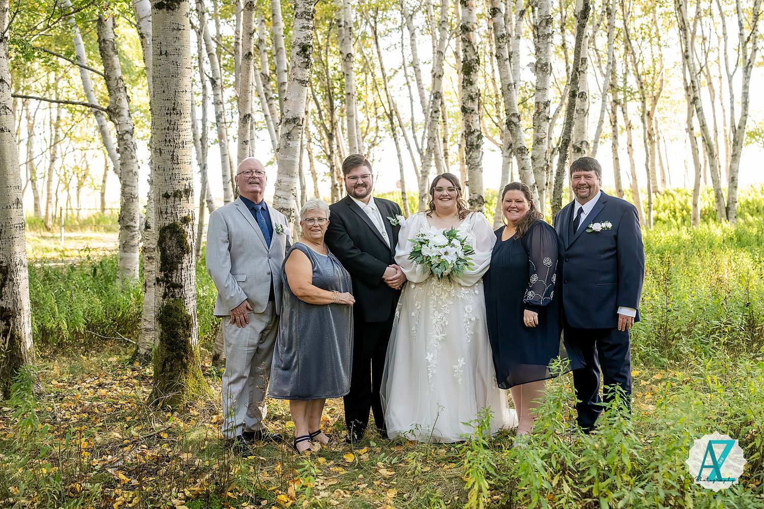 Group photo of wedding guests and party members standing among white birch trees in a natural forest setting.