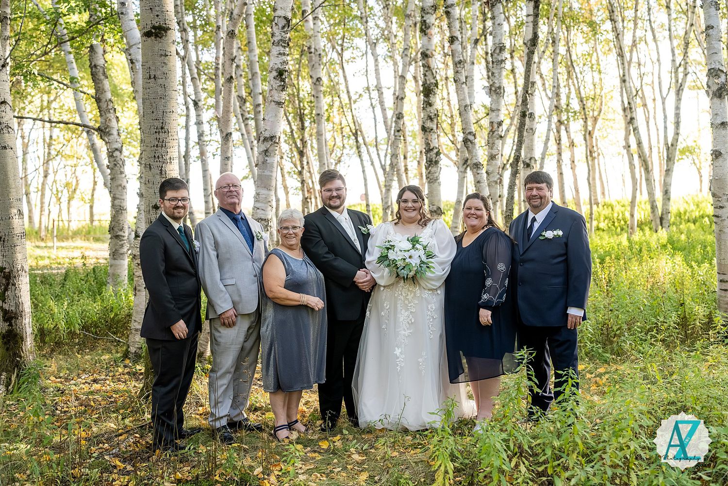 Large wedding group gathered in a serene aspen grove for formal photographs.