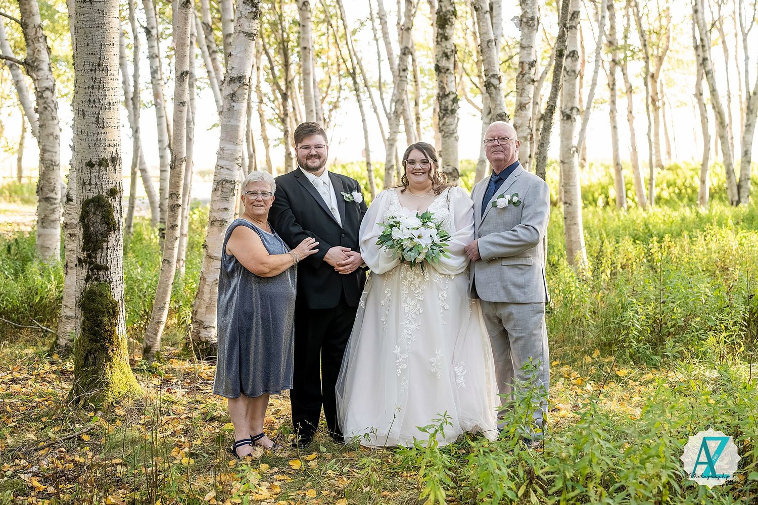 Wedding celebration group gathered among white birch trees in natural outdoor setting.