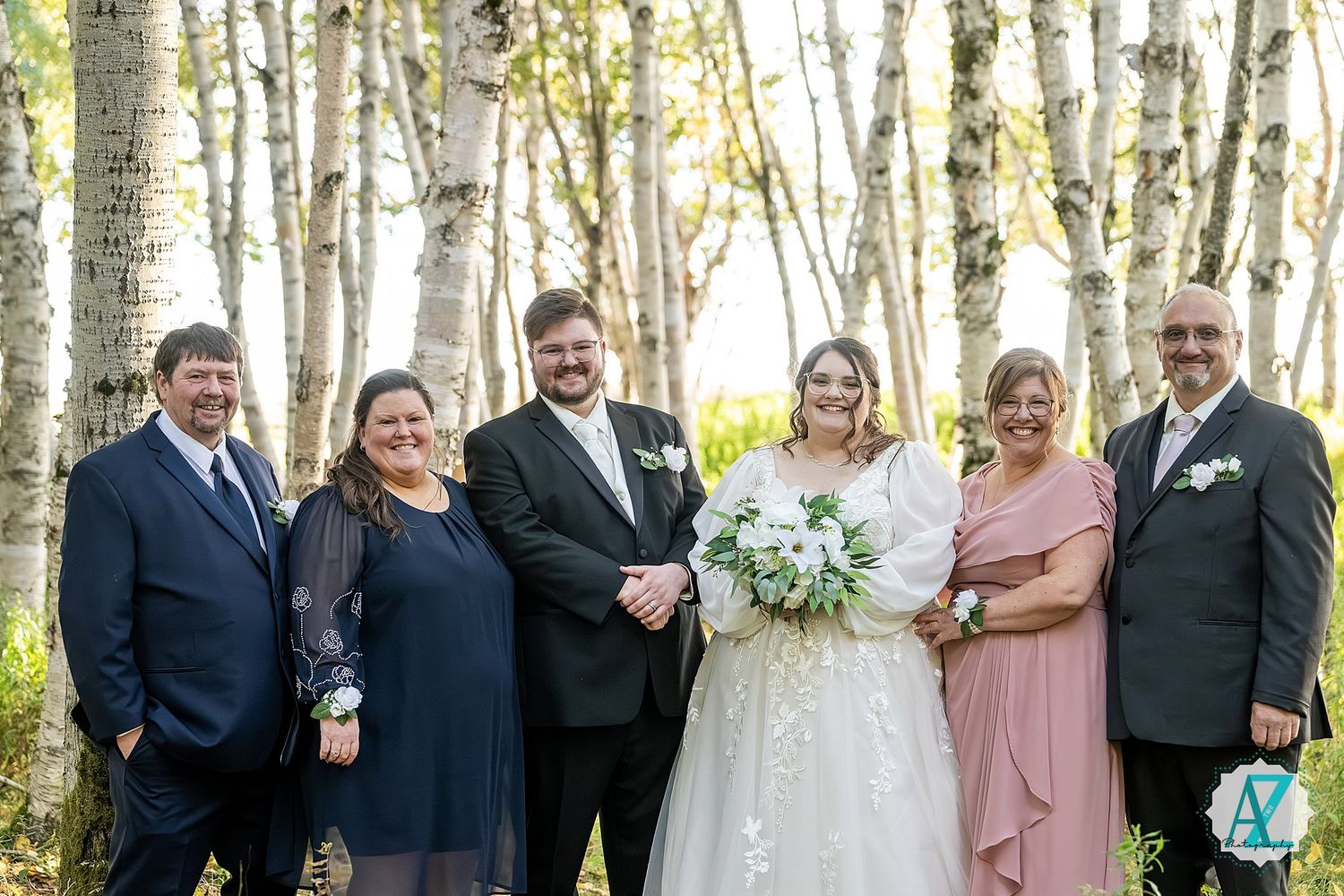 Wedding party in formal attire poses together among birch trees in a forest setting.