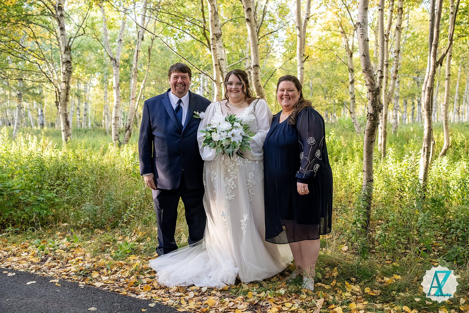 Wedding celebration group photo captured in a sun-dappled autumn forest setting.