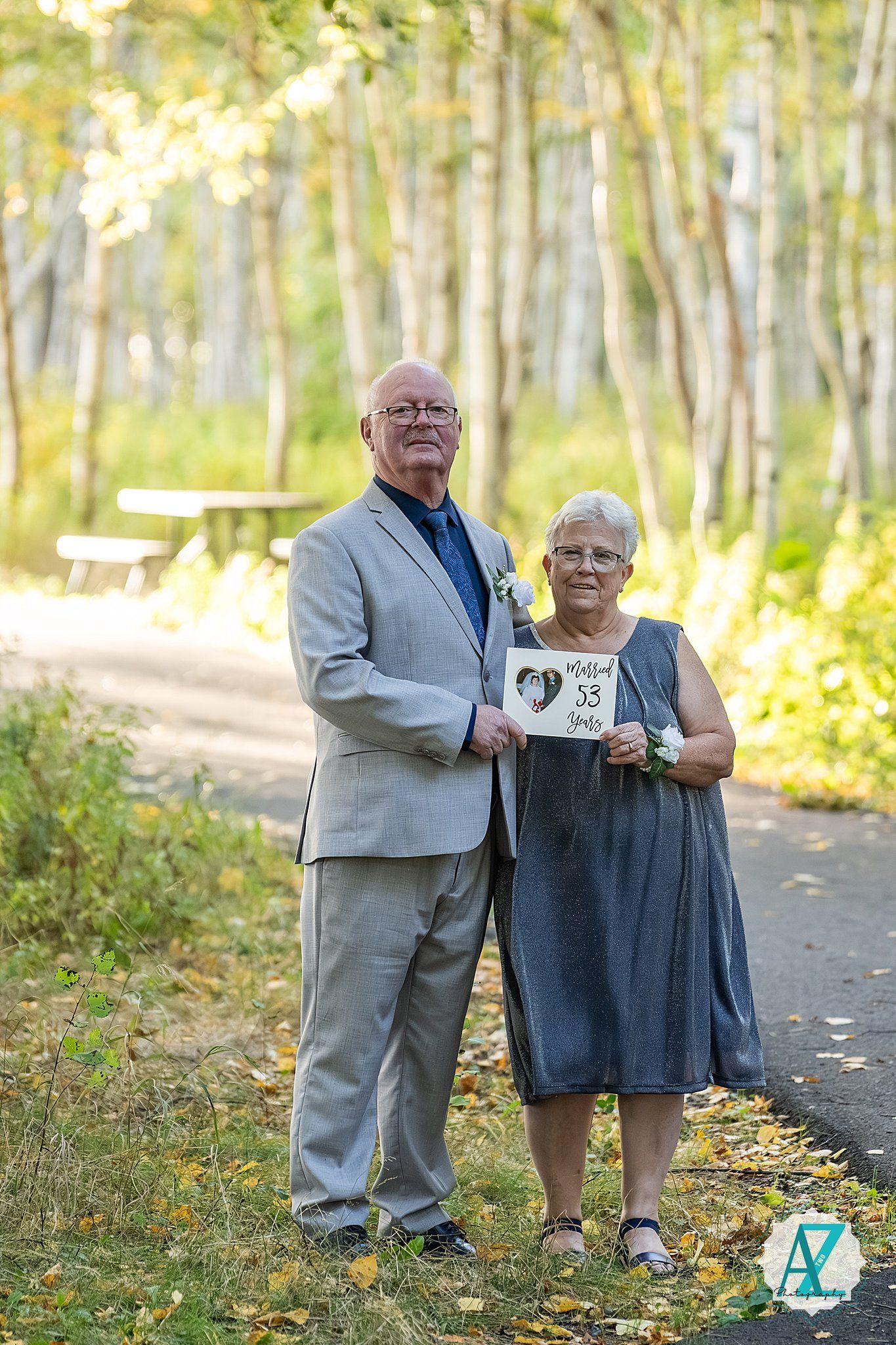 Couple poses together on a leaf-covered path in an autumn birch forest.